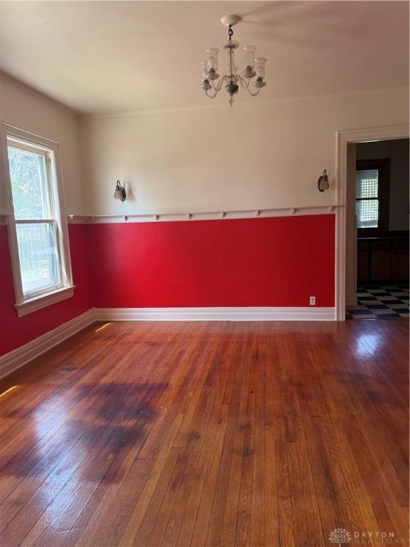 spare room with an inviting chandelier, hardwood / wood-style flooring, and baseboards