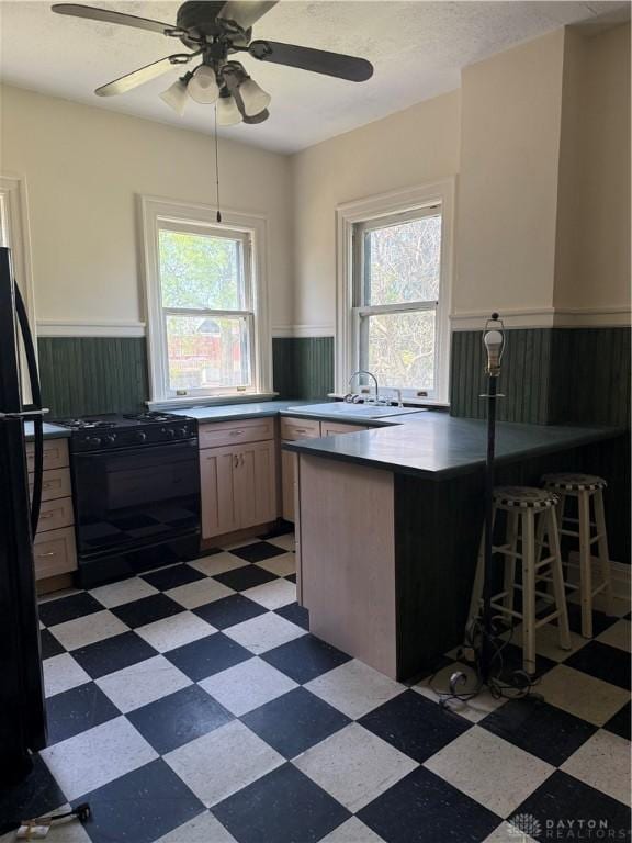 kitchen with light floors, plenty of natural light, wainscoting, black appliances, and a peninsula