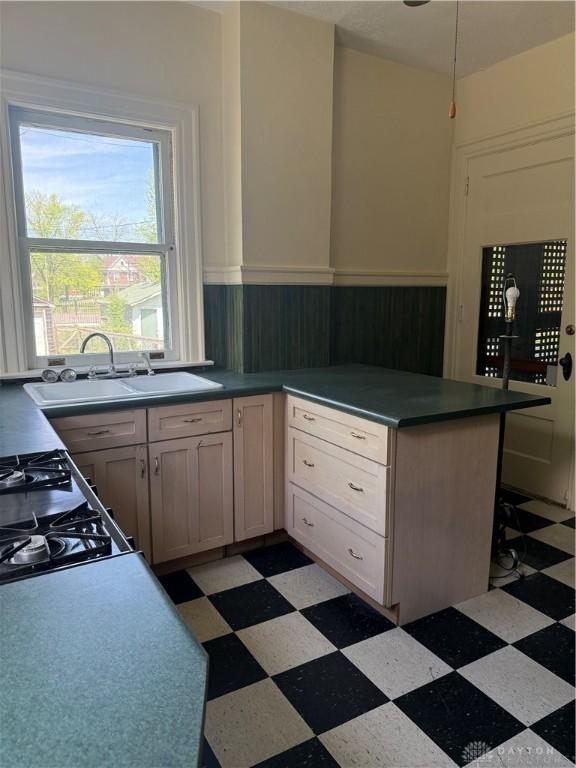 kitchen featuring a sink, wainscoting, a peninsula, and light floors