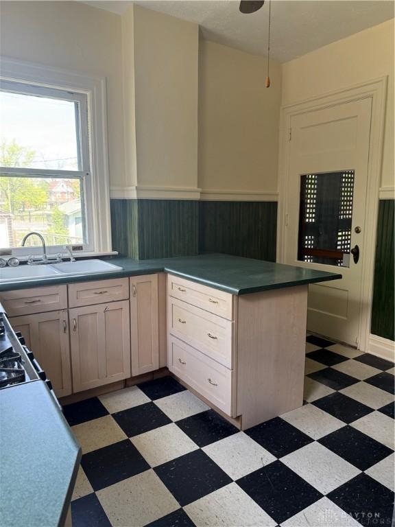 kitchen featuring a sink, wood walls, light floors, a peninsula, and wainscoting