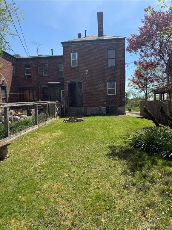 rear view of house with a lawn, brick siding, and fence