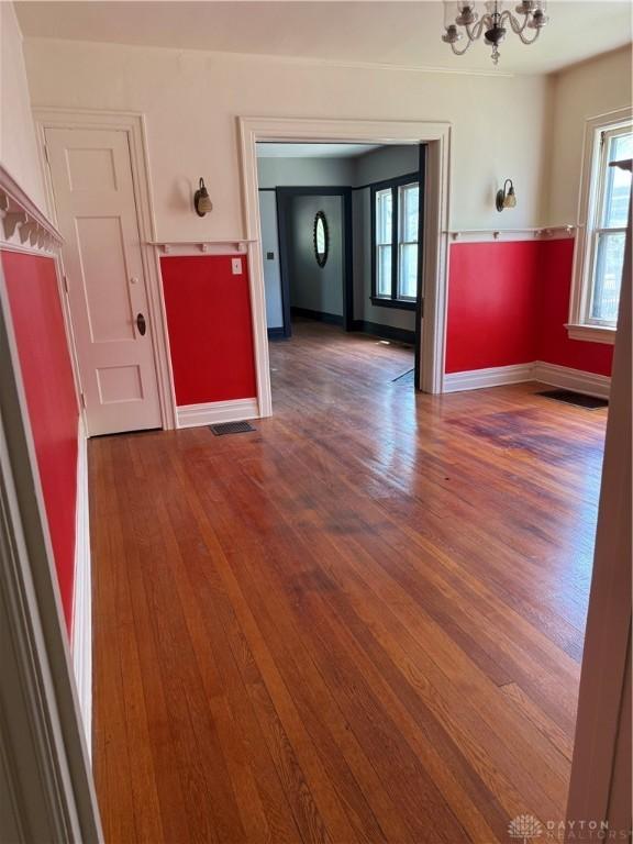 spare room featuring baseboards, visible vents, wood finished floors, and a notable chandelier