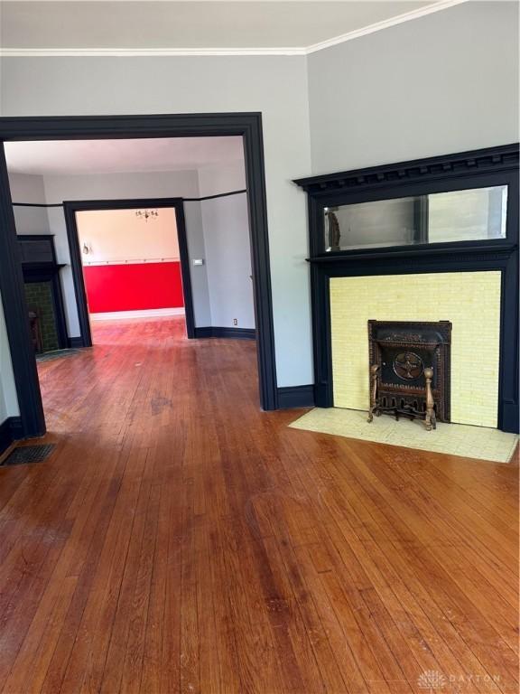 unfurnished living room with a fireplace, visible vents, baseboards, and wood-type flooring