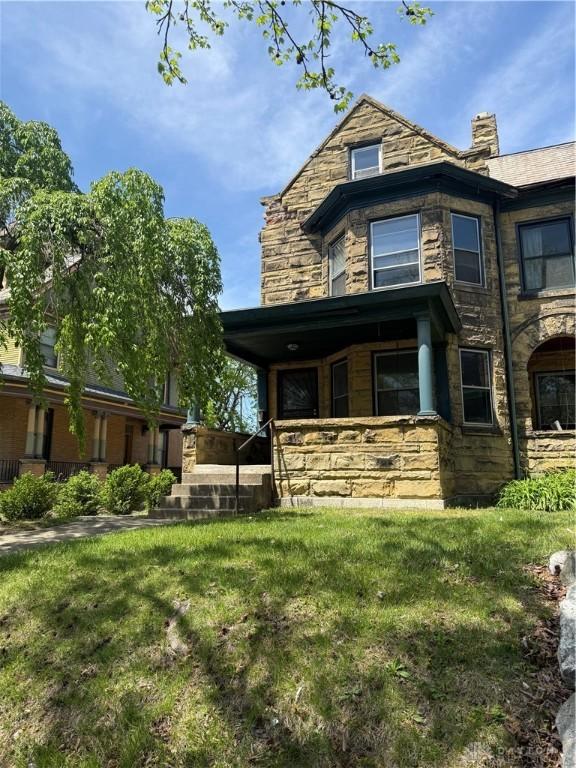 rear view of property with a yard, a porch, and stone siding