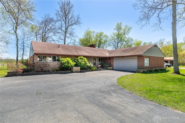 single story home with driveway, a chimney, a front yard, brick siding, and an attached garage