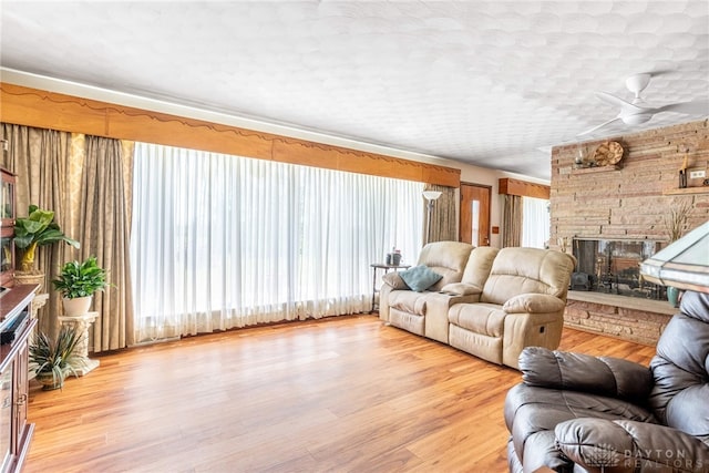 living area with a stone fireplace, light wood finished floors, and ceiling fan