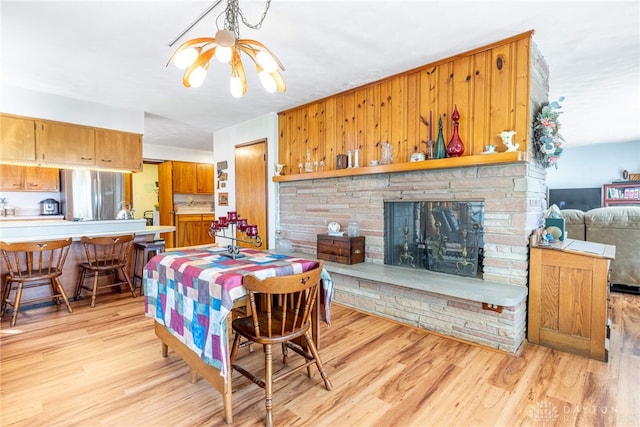 dining area featuring a fireplace, light wood-style flooring, and a notable chandelier