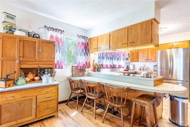 kitchen featuring light countertops, a breakfast bar, brown cabinetry, and light wood-type flooring