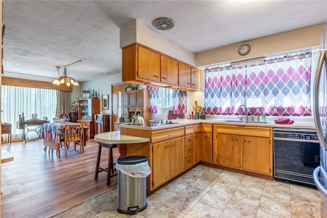 kitchen featuring brown cabinets, a sink, light countertops, a peninsula, and black appliances