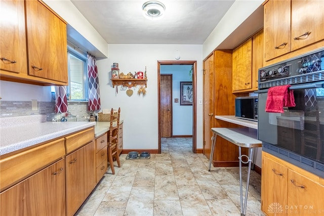kitchen with brown cabinetry, light countertops, baseboards, stainless steel microwave, and oven