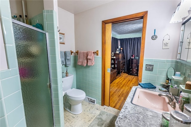full bath featuring tile walls, wainscoting, a stall shower, a sink, and toilet