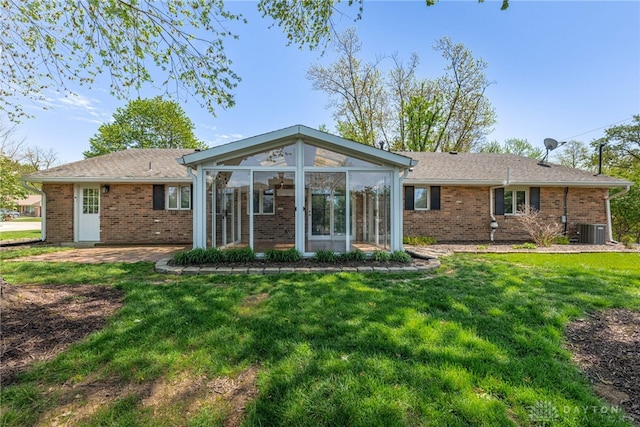 rear view of house featuring central air condition unit, brick siding, a sunroom, and a lawn