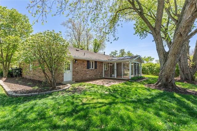 rear view of property with a sunroom, a patio area, a yard, and brick siding