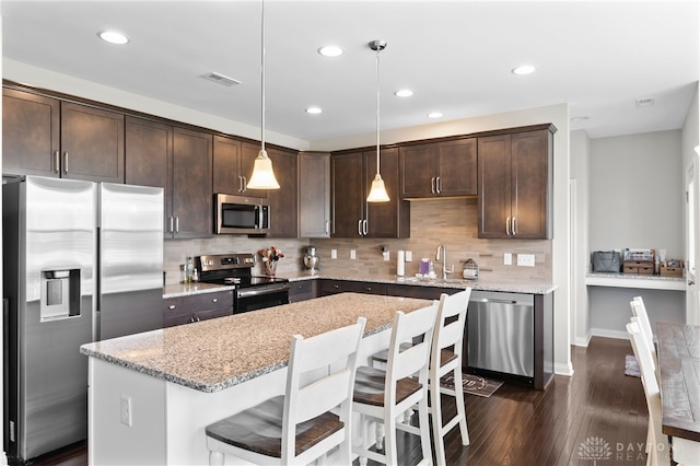 1621 Stonebury Ct, Xenia, OH 45385 - kitchen with stainless steel appliances, dark brown cabinets, dark wood-type flooring, a kitchen bar, and light stone countertops