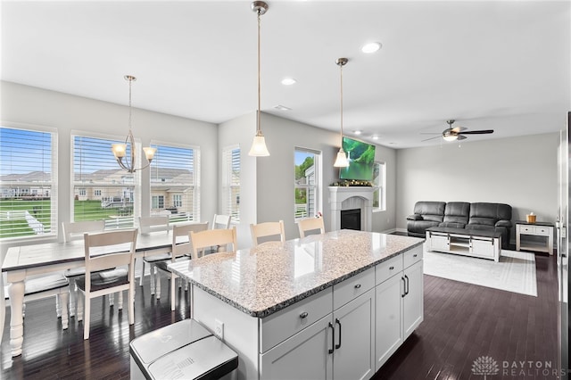 1621 Stonebury Ct, Xenia, OH 45385 - kitchen with a kitchen island, a fireplace, light stone counters, ceiling fan, and pendant lighting
