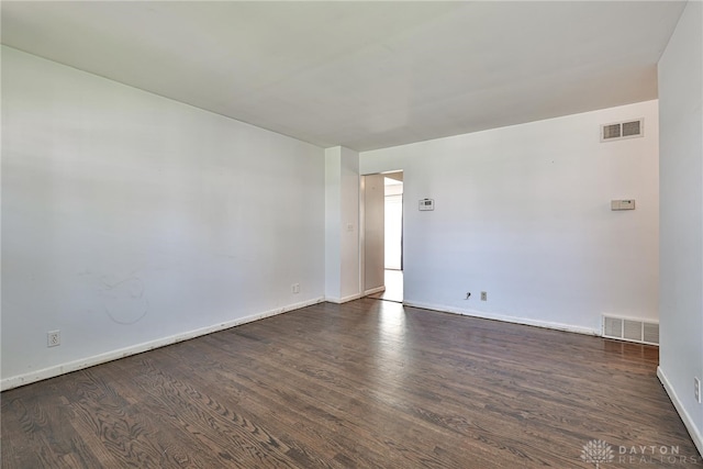 unfurnished room with baseboards, dark wood-type flooring, and visible vents