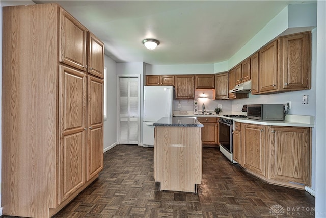 kitchen with range with gas cooktop, a kitchen island, stainless steel microwave, freestanding refrigerator, and under cabinet range hood