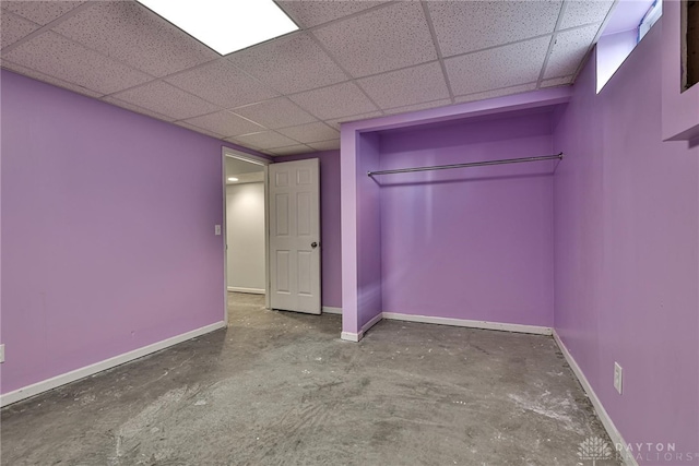 unfurnished bedroom featuring baseboards, unfinished concrete flooring, and a paneled ceiling