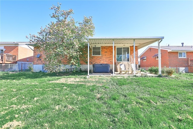 rear view of property with a hot tub, brick siding, a yard, and fence