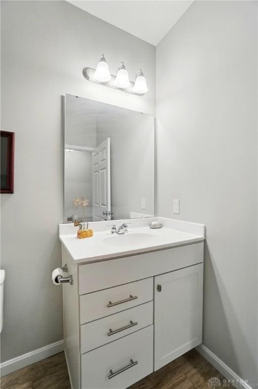half bathroom with toilet, baseboards, wood finished floors, and vanity