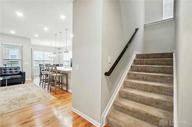 stairway with visible vents, wood finished floors, baseboards, recessed lighting, and a notable chandelier