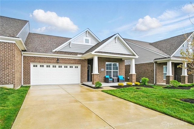 craftsman-style home featuring a shingled roof, brick siding, a garage, a front yard, and driveway