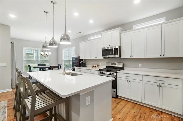 kitchen featuring appliances with stainless steel finishes, a sink, light wood-style floors, a kitchen breakfast bar, and an island with sink