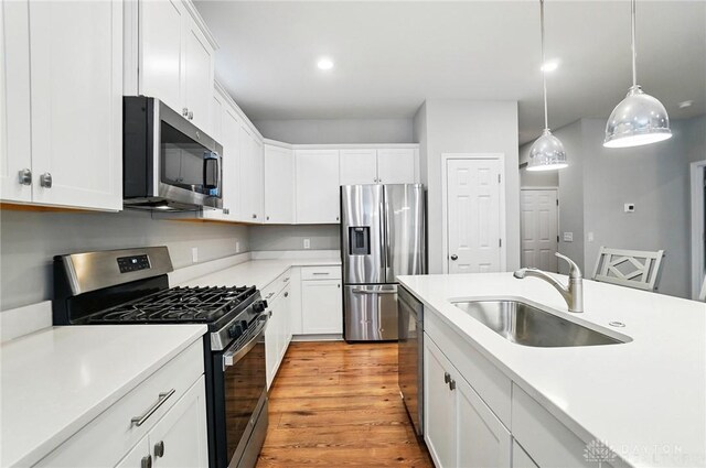 kitchen featuring hanging light fixtures, a sink, light countertops, stainless steel appliances, and white cabinetry