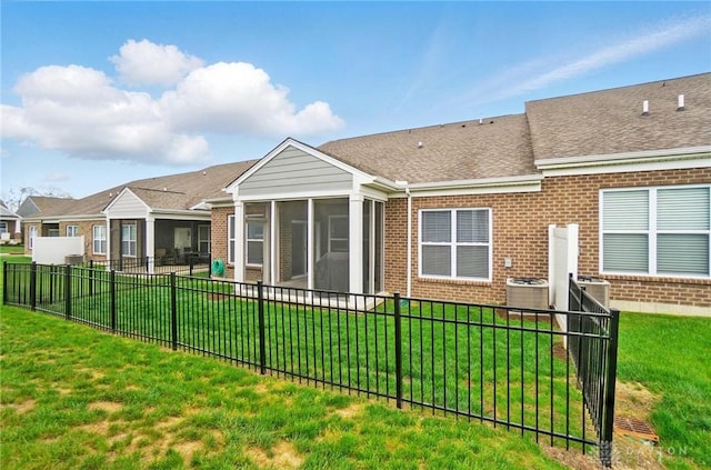 rear view of property with a shingled roof, brick siding, a sunroom, central air condition unit, and fence private yard