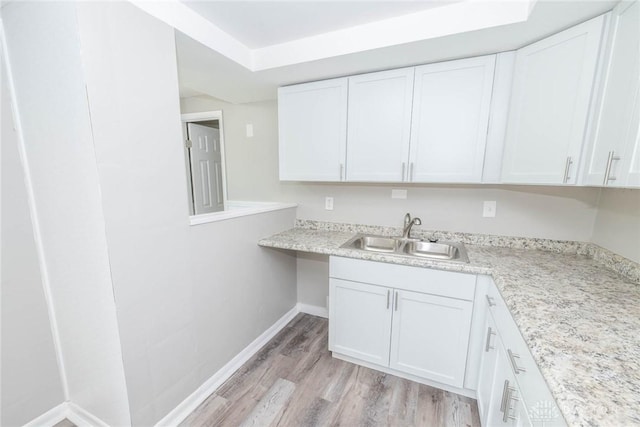 kitchen with white cabinets, a sink, light wood-style floors, light countertops, and baseboards