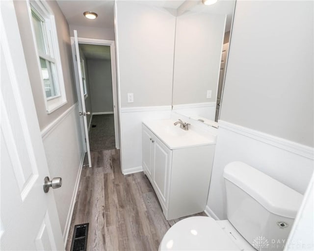bathroom with vanity, toilet, wood finished floors, and visible vents