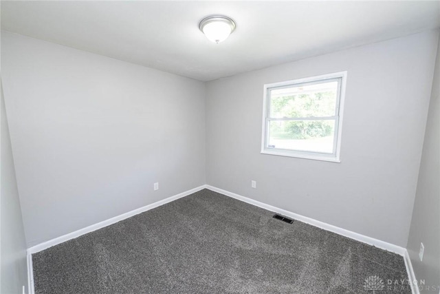 unfurnished room with visible vents, baseboards, and dark carpet