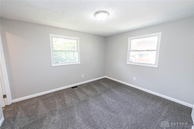 unfurnished room featuring a textured ceiling, baseboards, visible vents, and dark colored carpet