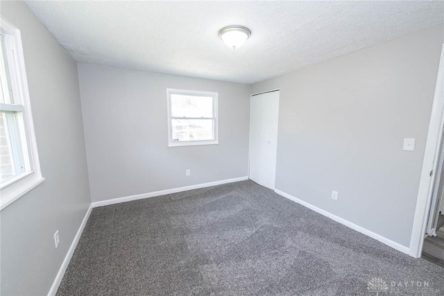 unfurnished bedroom with a textured ceiling, baseboards, dark carpet, and a closet