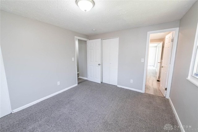 unfurnished bedroom featuring carpet floors, baseboards, a closet, and a textured ceiling