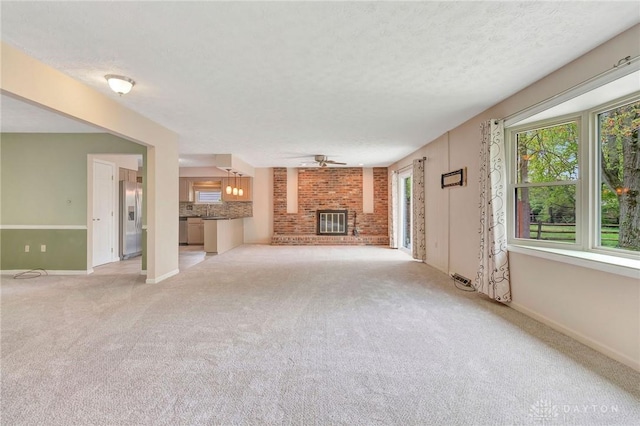 unfurnished living room featuring a brick fireplace, baseboards, light colored carpet, a textured ceiling, and a ceiling fan