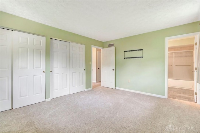 unfurnished bedroom with carpet flooring, connected bathroom, multiple closets, baseboards, and visible vents