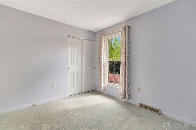 empty room with baseboards, light carpet, a textured ceiling, and visible vents