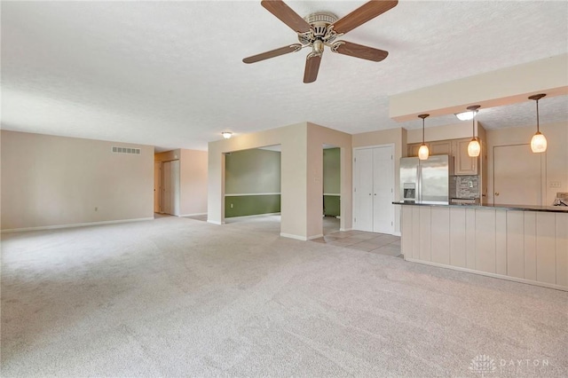 unfurnished living room with visible vents, baseboards, ceiling fan, light colored carpet, and a textured ceiling