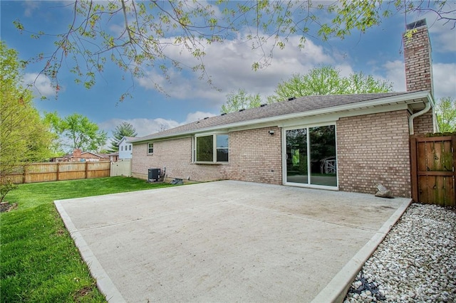 back of house with a fenced backyard, a chimney, a lawn, and brick siding