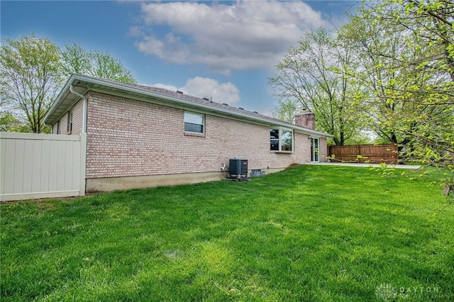 rear view of property featuring a chimney, central AC unit, brick siding, fence, and a yard