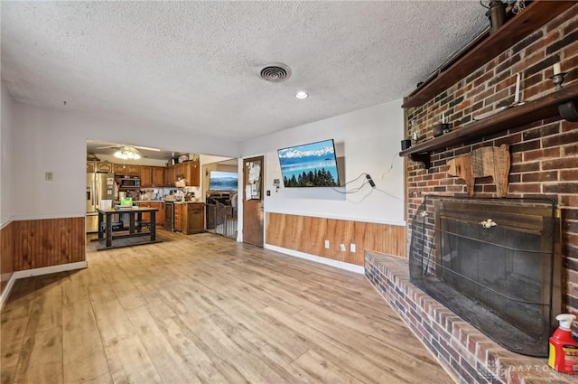 1015 Colorado Dr, Xenia, OH 45385 - living room featuring wainscoting, a textured ceiling, light wood finished floors, wooden walls, and a brick fireplace