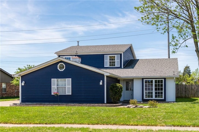 traditional-style house featuring roof with shingles, fence, and a front yard