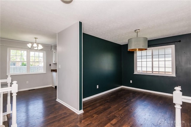 unfurnished room featuring a textured ceiling, a chandelier, baseboards, wood finished floors, and visible vents