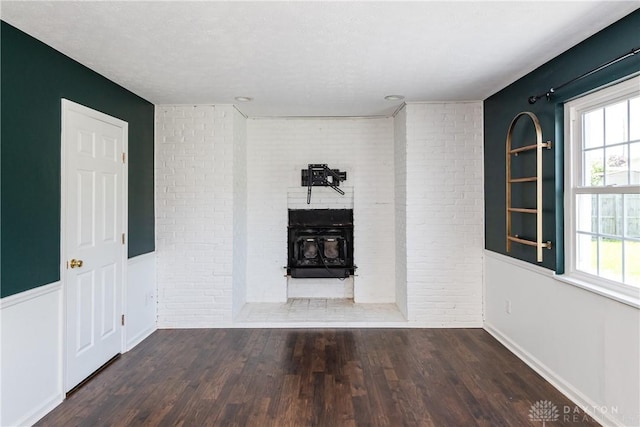 unfurnished living room featuring baseboards, brick wall, wood finished floors, and a fireplace