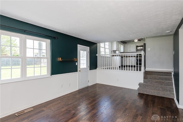 unfurnished living room with visible vents, baseboards, stairway, a ceiling fan, and dark wood finished floors