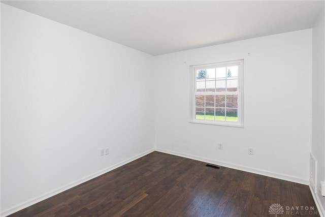 empty room featuring dark wood-type flooring, baseboards, and visible vents