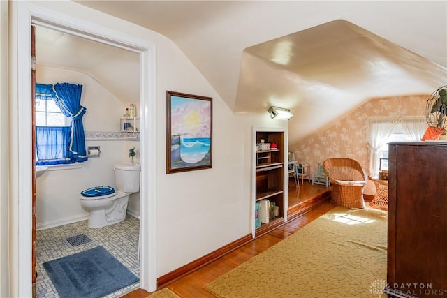 corridor featuring baseboards, wallpapered walls, wood finished floors, and lofted ceiling