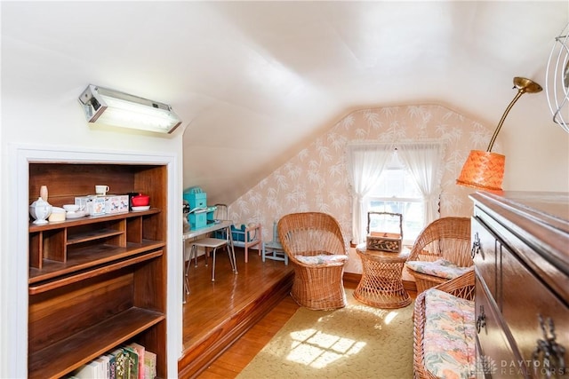 sitting room with wallpapered walls, wood finished floors, and lofted ceiling