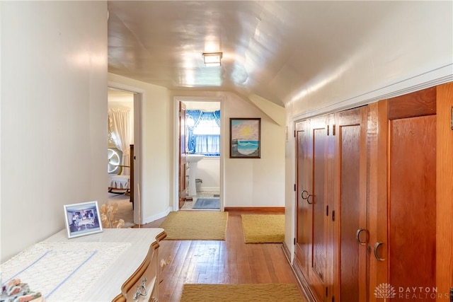 hallway featuring baseboards, lofted ceiling, and light wood-type flooring